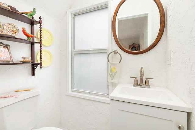 bathroom featuring a textured wall, vanity, and toilet