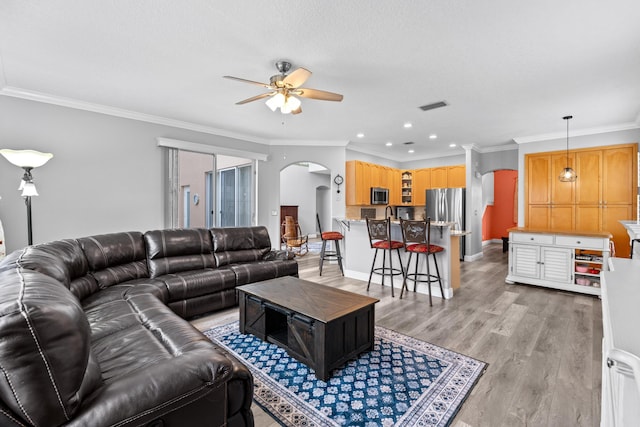 living room with visible vents, arched walkways, light wood-style floors, crown molding, and ceiling fan