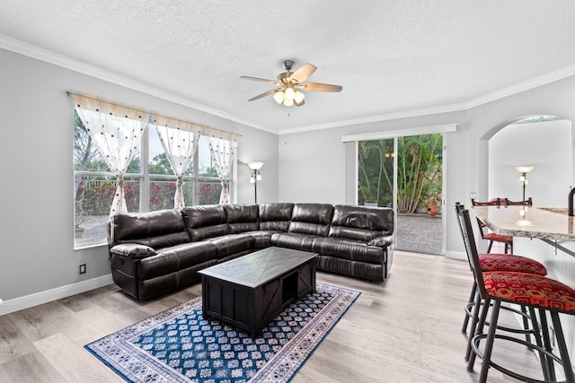 living room featuring arched walkways, a textured ceiling, ornamental molding, and light wood finished floors