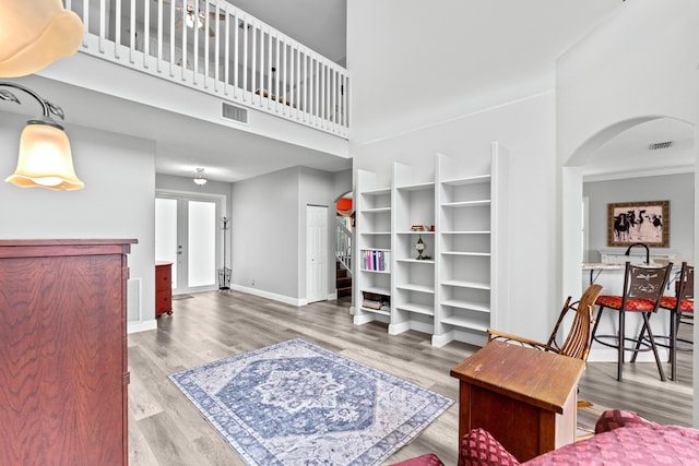 living area featuring wood finished floors, visible vents, baseboards, a high ceiling, and arched walkways