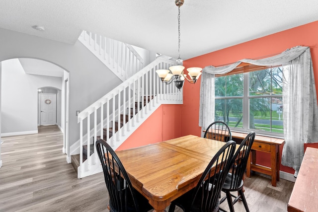 dining space featuring a notable chandelier, arched walkways, light wood finished floors, baseboards, and stairs