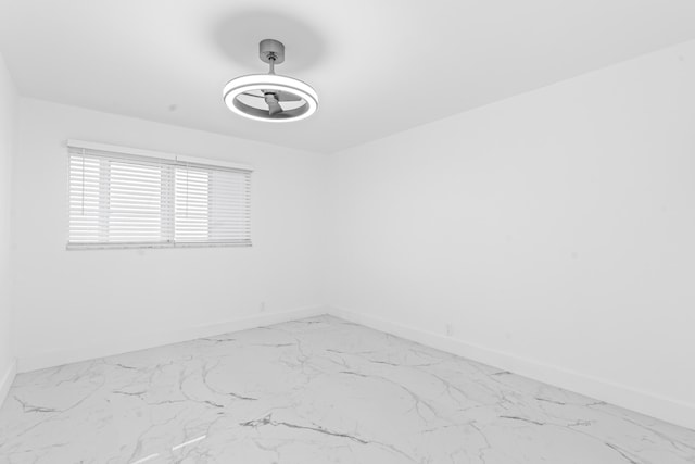 empty room featuring a ceiling fan, marble finish floor, and baseboards