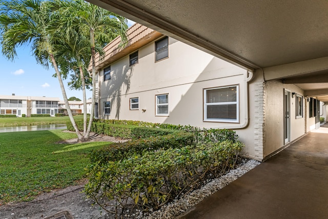 view of side of home featuring a yard, a water view, a tiled roof, and stucco siding