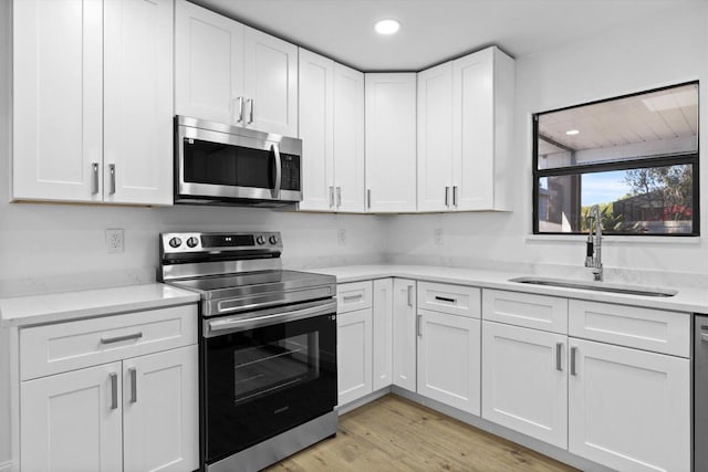 kitchen featuring stainless steel appliances, a sink, white cabinetry, light countertops, and light wood finished floors