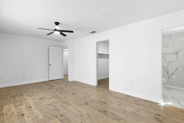 unfurnished bedroom featuring visible vents, a spacious closet, ensuite bathroom, wood finished floors, and baseboards