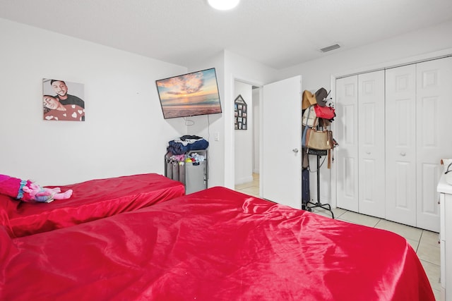 bedroom with light tile patterned floors, visible vents, and a closet