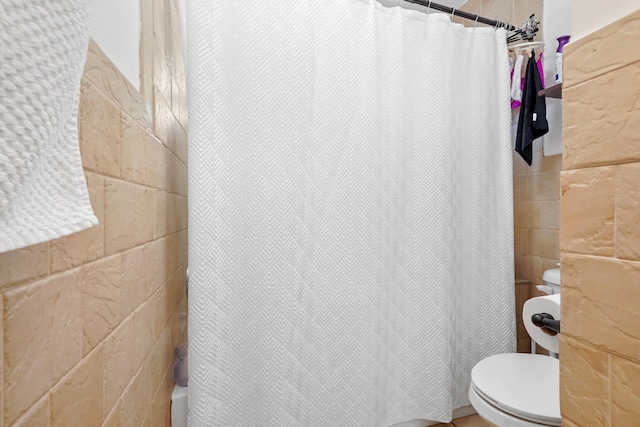 bathroom featuring toilet and tile walls