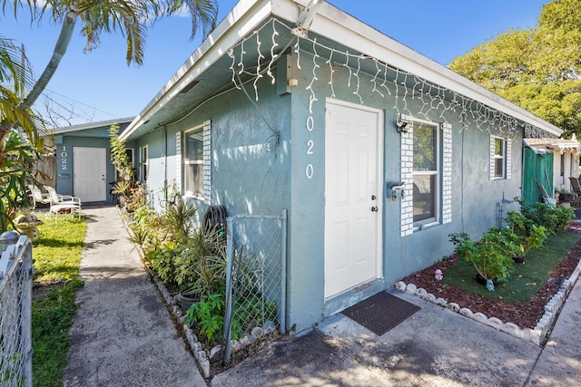 view of exterior entry with stucco siding and fence