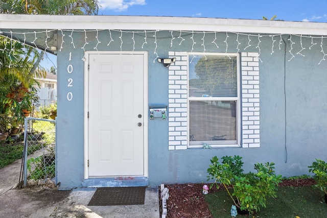 property entrance featuring stucco siding, brick siding, and fence