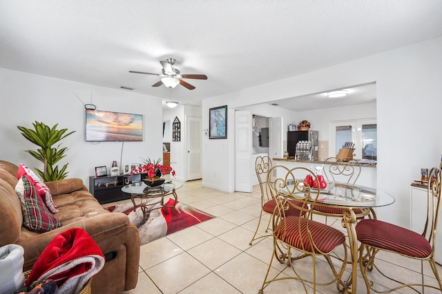 living area featuring light tile patterned floors, visible vents, a textured ceiling, and a ceiling fan