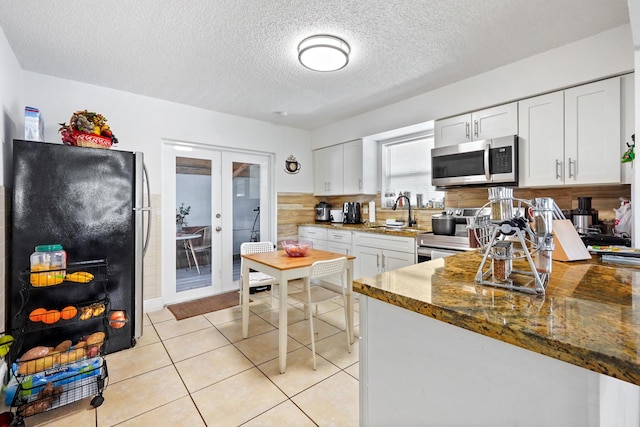 kitchen featuring dark stone countertops, light tile patterned floors, stainless steel appliances, french doors, and white cabinetry