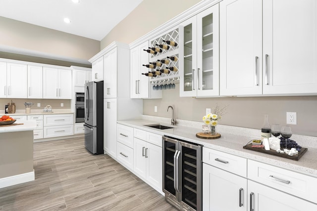 kitchen featuring beverage cooler, white cabinets, a sink, and freestanding refrigerator