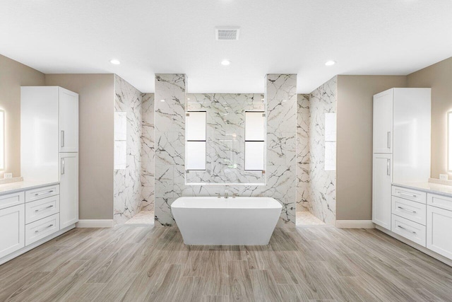 bathroom featuring wood finished floors, vanity, visible vents, a freestanding bath, and a marble finish shower