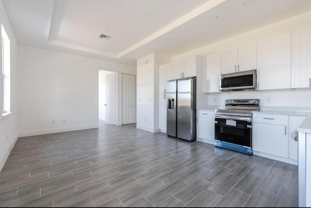 kitchen featuring stainless steel appliances, visible vents, white cabinetry, light countertops, and a tray ceiling