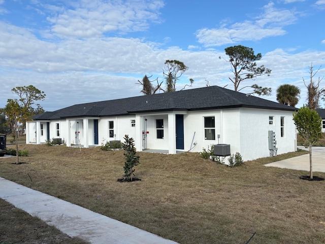 ranch-style house featuring roof with shingles, central AC, a front lawn, and stucco siding