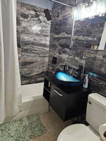 bathroom featuring shower / bath combination with curtain, tile walls, vanity, and toilet