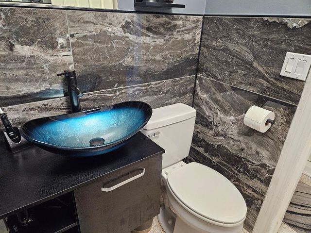 bathroom with toilet, tile walls, and vanity