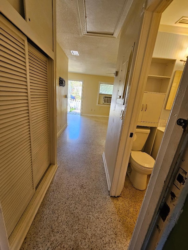 hallway with a textured ceiling, speckled floor, visible vents, baseboards, and attic access