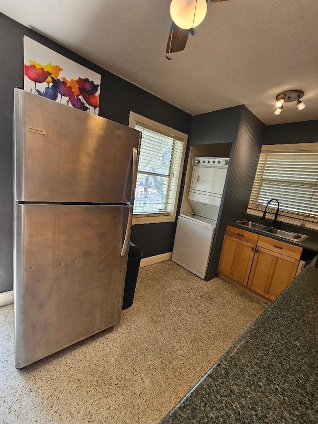 kitchen featuring a sink, a ceiling fan, baseboards, freestanding refrigerator, and brown cabinetry