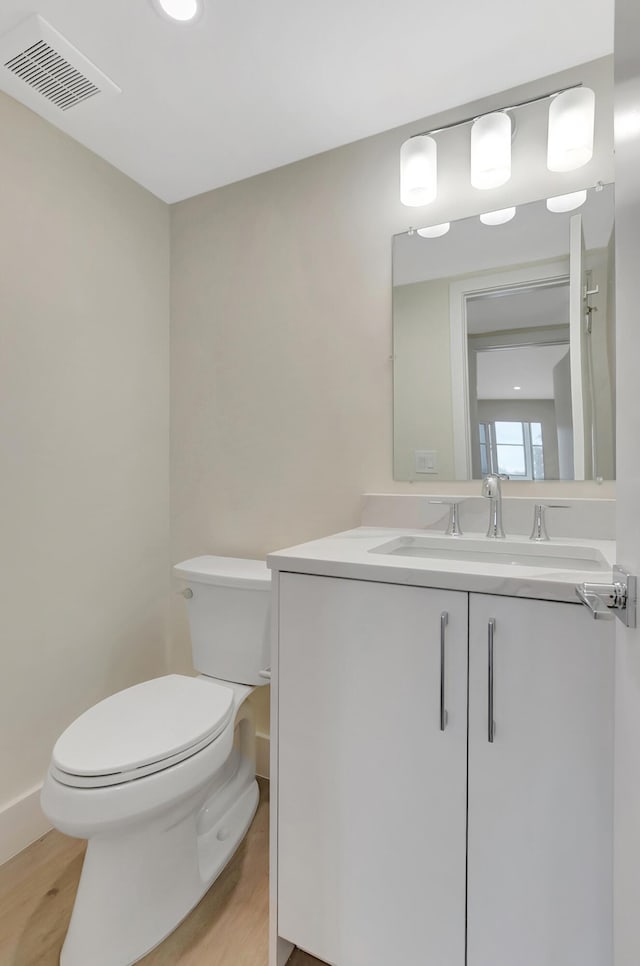 half bath featuring vanity, toilet, wood finished floors, and visible vents