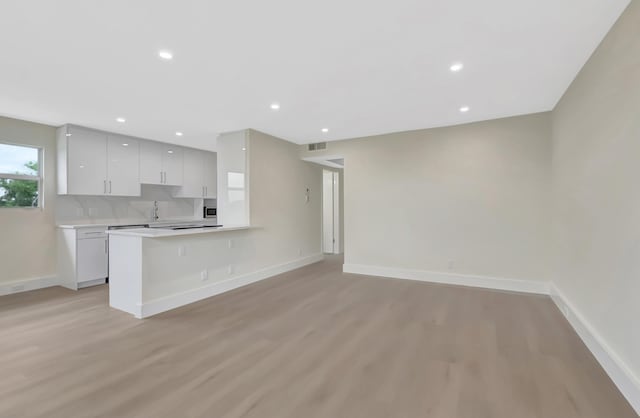 kitchen featuring light wood finished floors, visible vents, baseboards, light countertops, and decorative backsplash