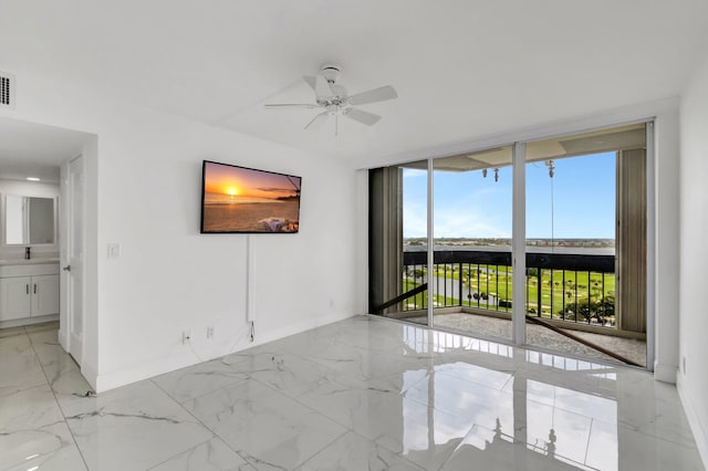 empty room with visible vents, a ceiling fan, baseboards, marble finish floor, and a wall of windows