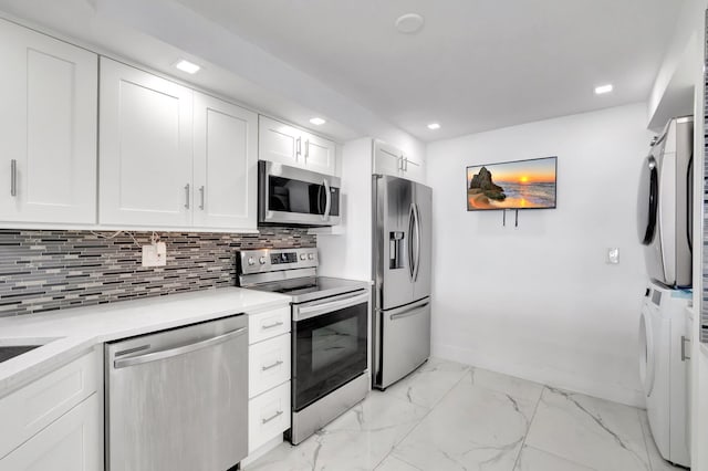 kitchen featuring stainless steel appliances, white cabinetry, marble finish floor, stacked washing maching and dryer, and backsplash