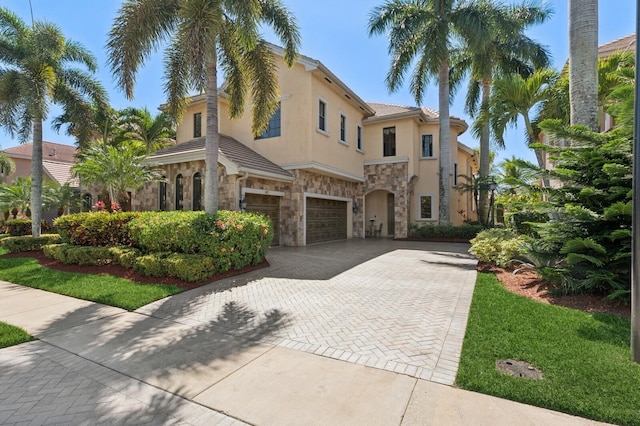 mediterranean / spanish house featuring stucco siding, a garage, stone siding, a tile roof, and decorative driveway