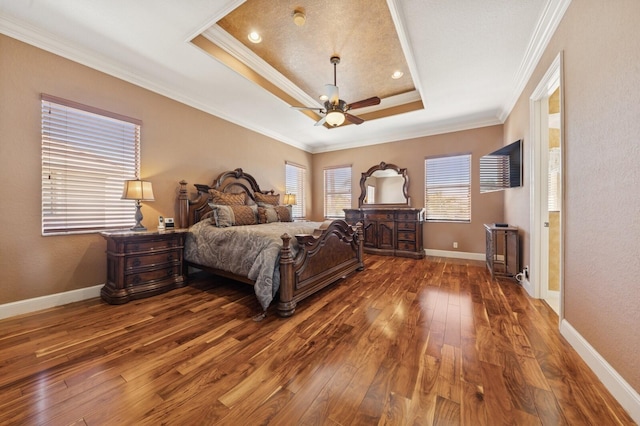 bedroom with baseboards, ornamental molding, hardwood / wood-style flooring, a raised ceiling, and a ceiling fan