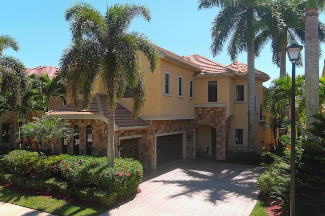 mediterranean / spanish-style home featuring a tile roof, stucco siding, decorative driveway, a garage, and stone siding