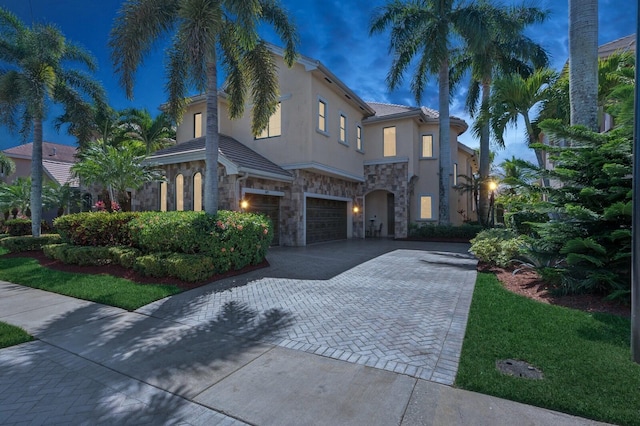 mediterranean / spanish home featuring driveway, an attached garage, stucco siding, stone siding, and a tile roof