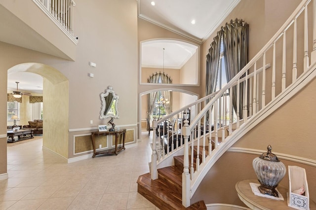 staircase with arched walkways, ceiling fan, a towering ceiling, crown molding, and tile patterned floors