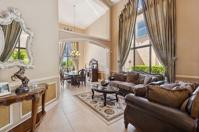 living room featuring a wainscoted wall, ornamental molding, a high ceiling, an inviting chandelier, and light tile patterned floors