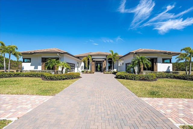 prairie-style house featuring stucco siding, an attached garage, decorative driveway, and a front lawn