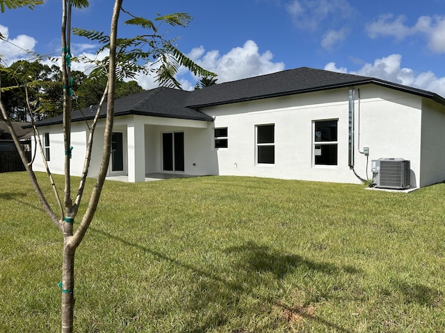 back of property featuring central air condition unit, stucco siding, a shingled roof, and a yard