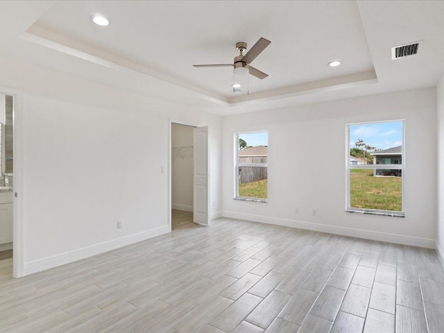 unfurnished bedroom with a tray ceiling, a walk in closet, visible vents, and baseboards