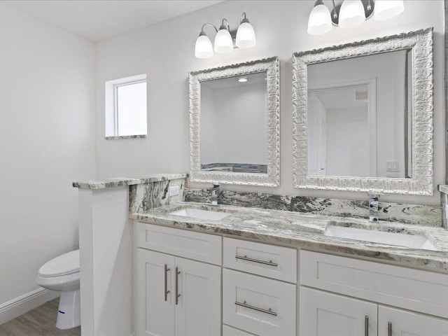 bathroom featuring wood finished floors, a sink, toilet, and double vanity