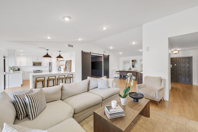 living room featuring a barn door, recessed lighting, visible vents, vaulted ceiling, and light wood finished floors