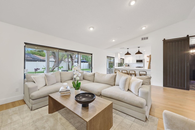 living area featuring lofted ceiling, recessed lighting, visible vents, light wood-style flooring, and a barn door