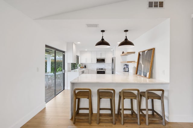 kitchen with stainless steel appliances, light countertops, visible vents, white cabinetry, and a peninsula