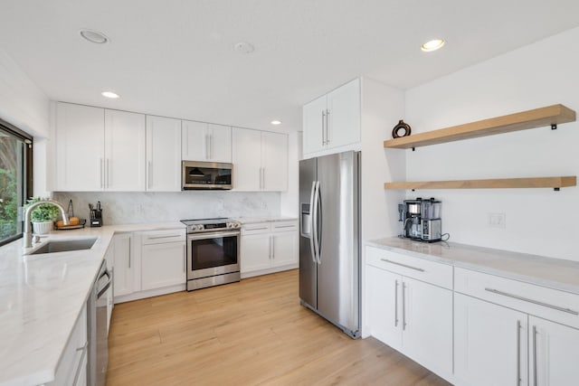 kitchen featuring tasteful backsplash, appliances with stainless steel finishes, light wood-style floors, open shelves, and a sink