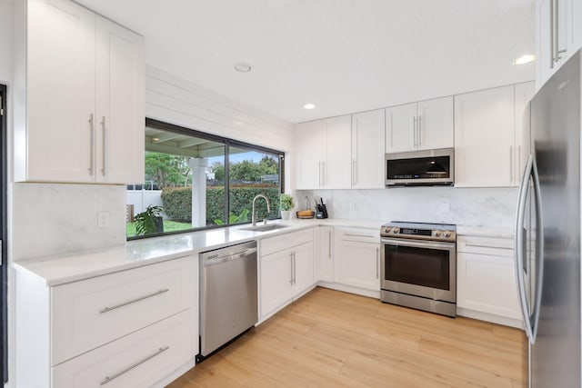 kitchen featuring appliances with stainless steel finishes, light wood-type flooring, white cabinets, and a sink