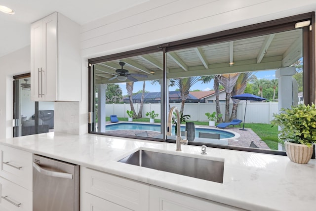 kitchen with dishwasher, a sink, white cabinetry, and light stone countertops