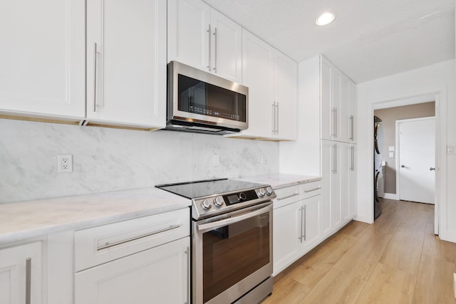 kitchen featuring light wood finished floors, appliances with stainless steel finishes, white cabinets, and stacked washer / drying machine