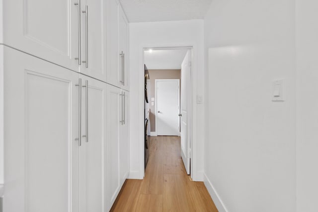 corridor with light wood-type flooring, a textured ceiling, and baseboards