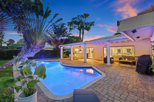 pool at dusk with outdoor lounge area, a patio, grilling area, and ceiling fan