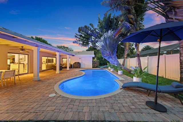 pool at dusk with a patio, fence, a ceiling fan, and a fenced in pool