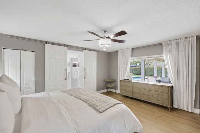 bedroom featuring a barn door, ceiling fan, a textured ceiling, light wood-type flooring, and baseboards