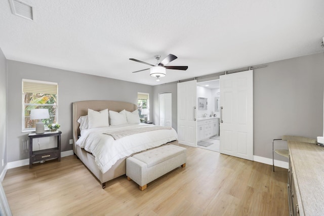 bedroom featuring visible vents, a barn door, a textured ceiling, light wood-type flooring, and baseboards