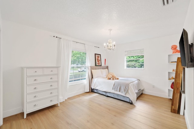 bedroom featuring a chandelier, a textured ceiling, light wood-style flooring, visible vents, and baseboards